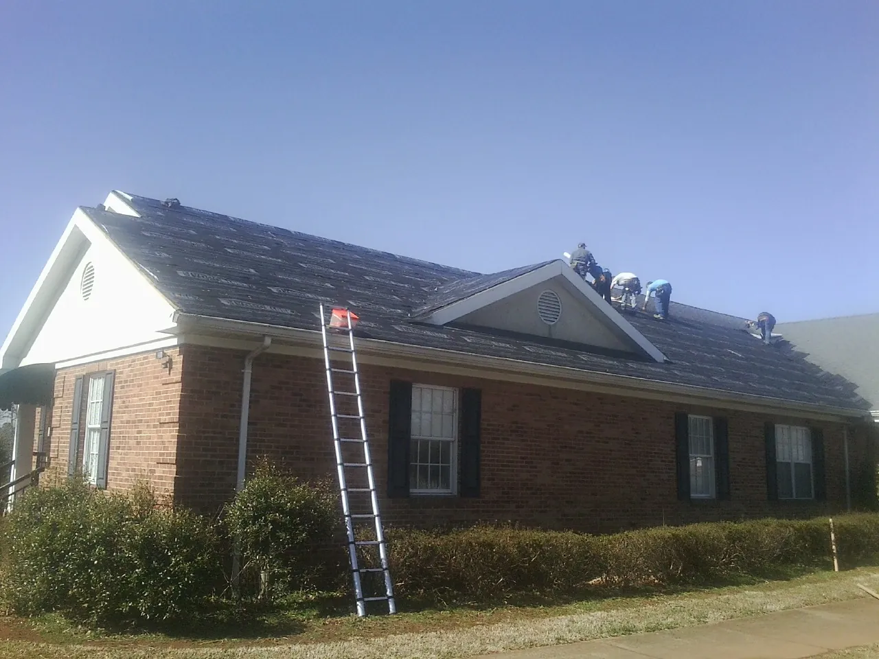 Crew tearing shingles off a brick ranch roof with a ladder set — Metal Roof Repair work by our crew in Shenandoah