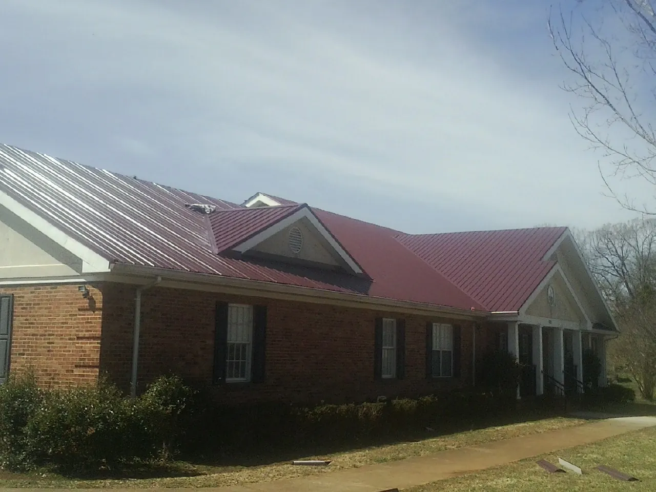Red metal roof with gabled entries on a long brick building, from a Hail Damage Roof Repair job in Shenandoah