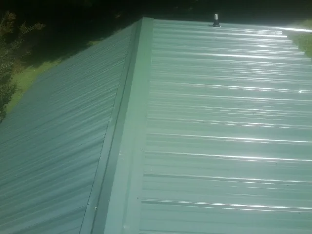 New green metal panels meeting at the ridge of a roof — Flat Roof Repair work by our crew in Shenandoah