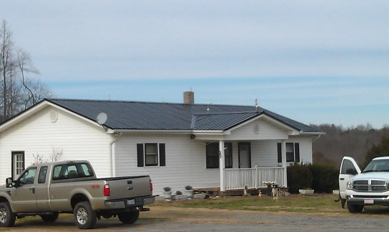 Finished dark metal roof on a white ranch home with work trucks parked in Shenandoah