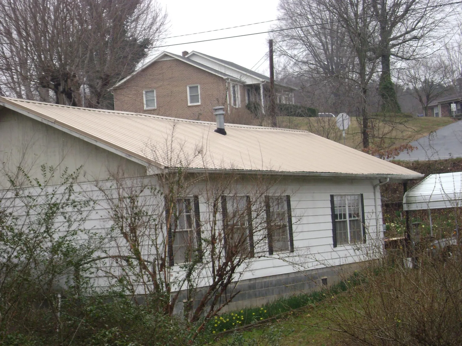 Tan metal roof on a white sided house set into a hillside — Commercial Roofing by Roofing Brothers in Shenandoah