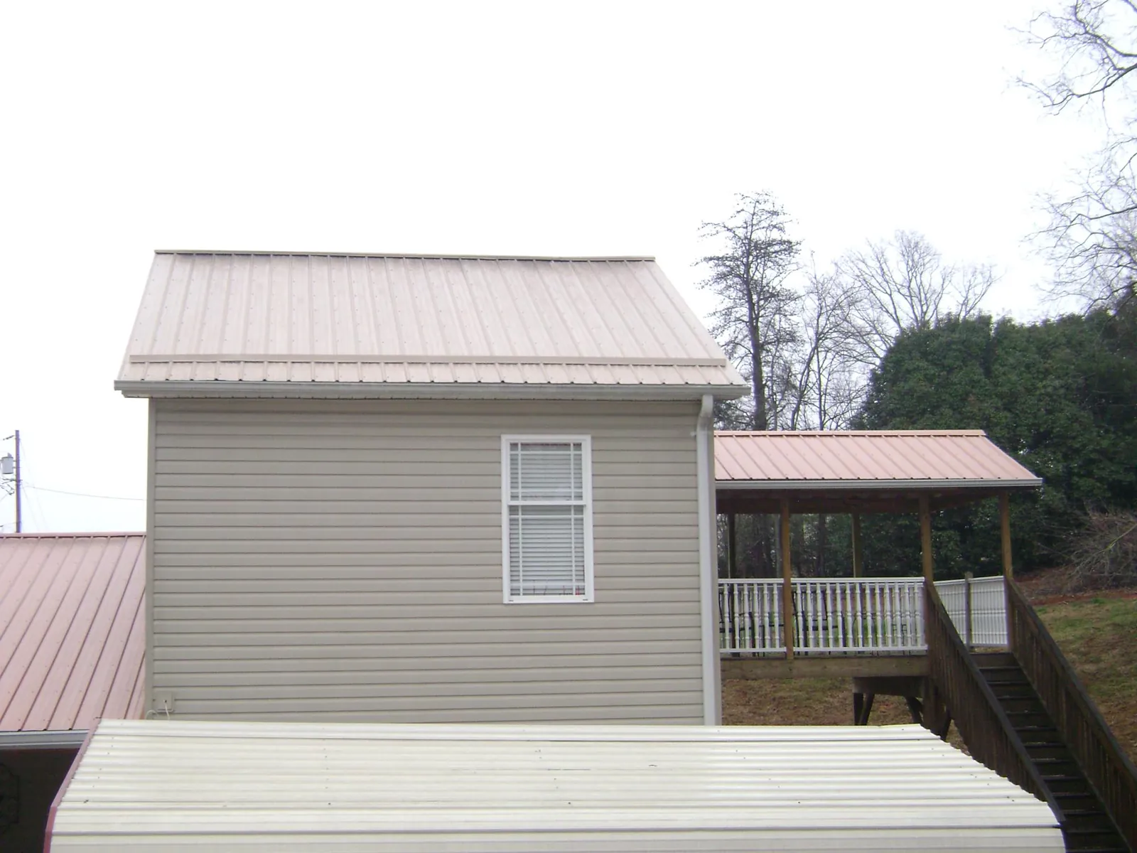 Tan metal roofs on a two story addition and attached porch, from a Roof Replacement job in Shenandoah